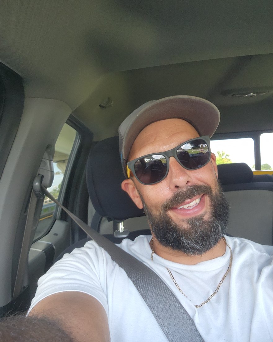 Rob behind the wheel — cap, sunglasses, seatbelt on, grinning